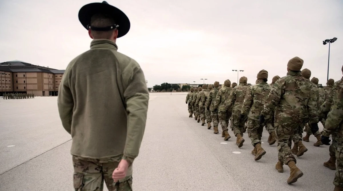 Military training instructor in a campaign hat beside a marching recruit flight