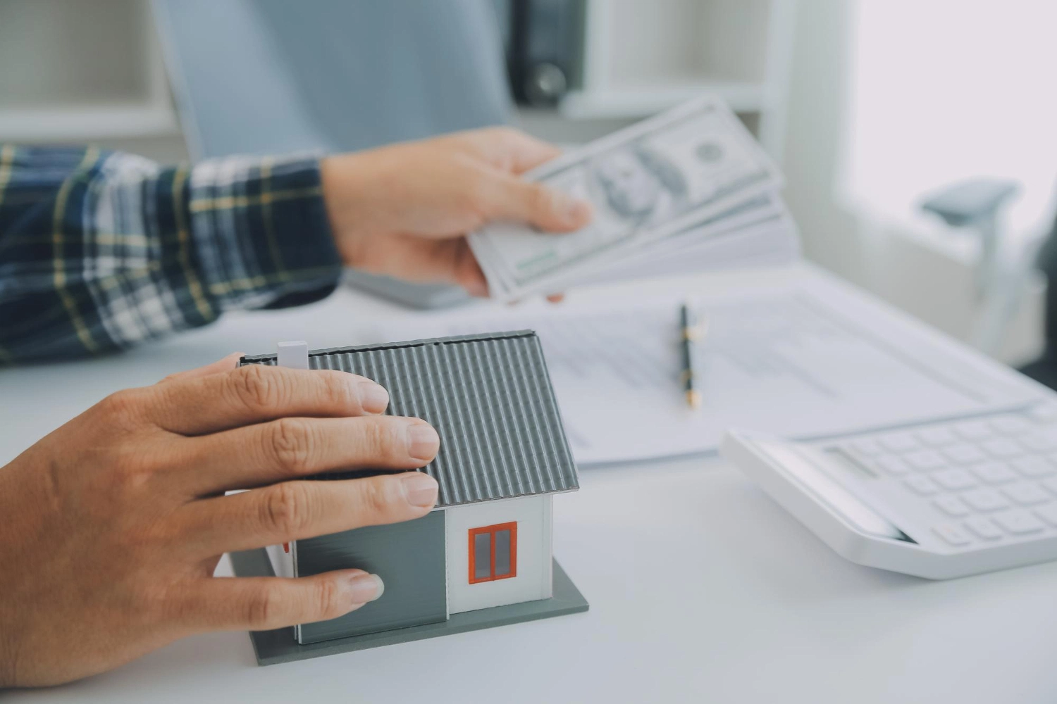 Hands passing a house model over paperwork, representing a drop in BAH rates