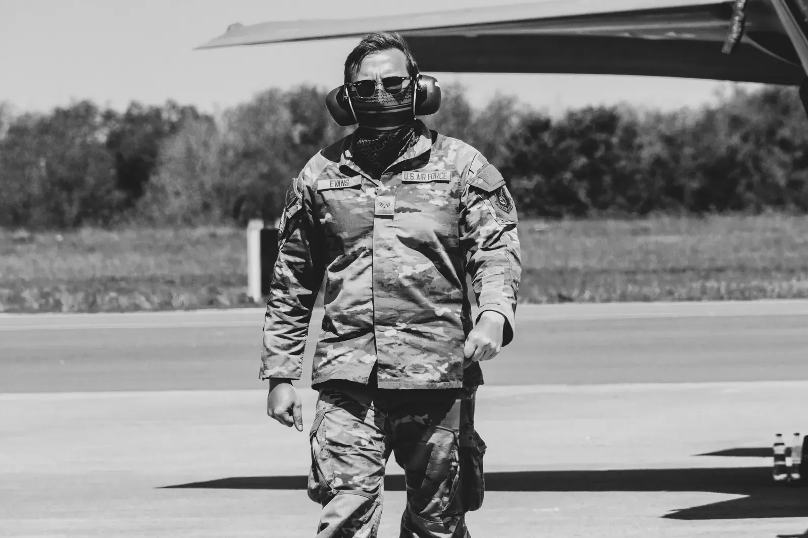 Airman in uniform walking across a flight line past a military aircraft