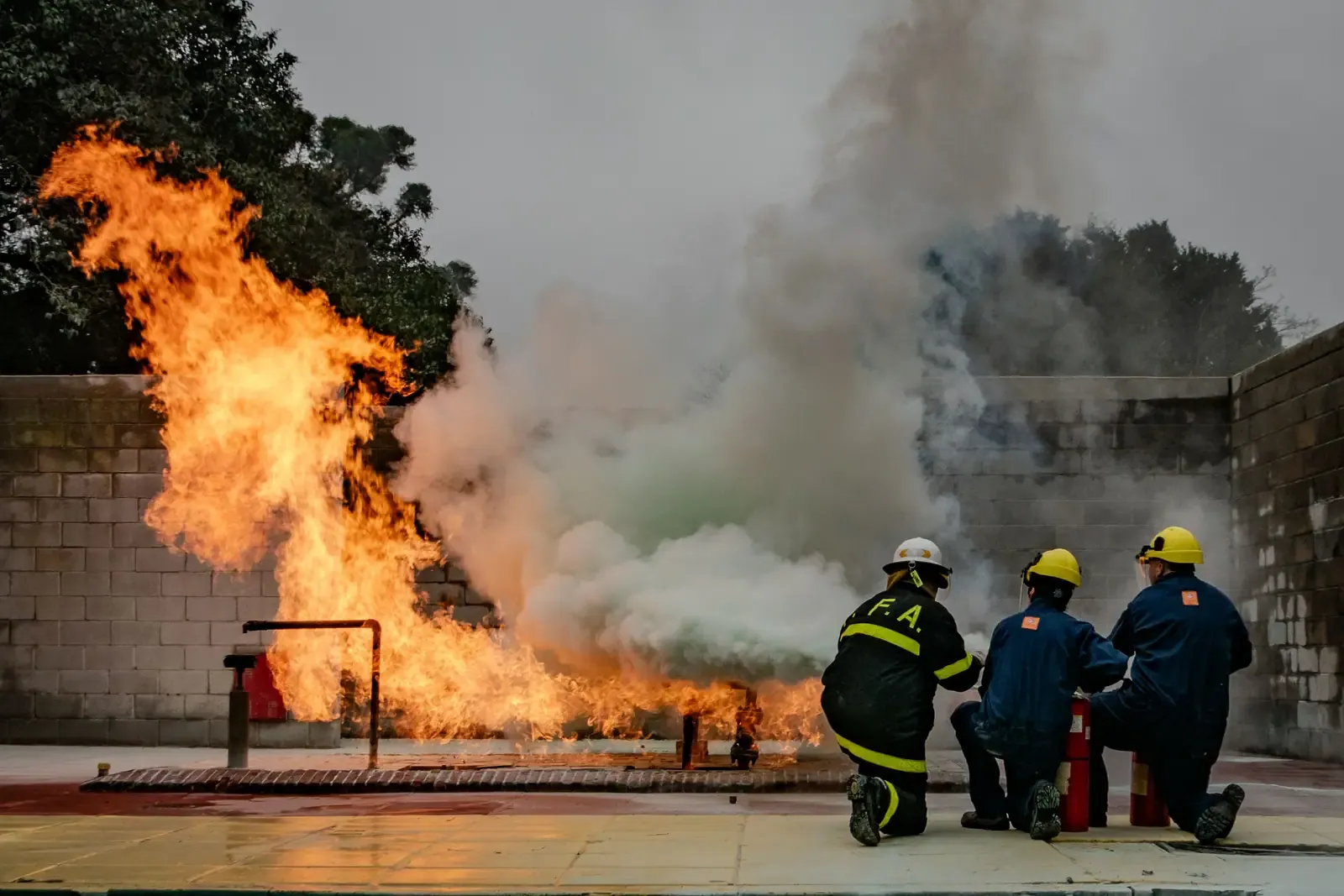 Trainees in fire gear fighting a live training fire with a hose