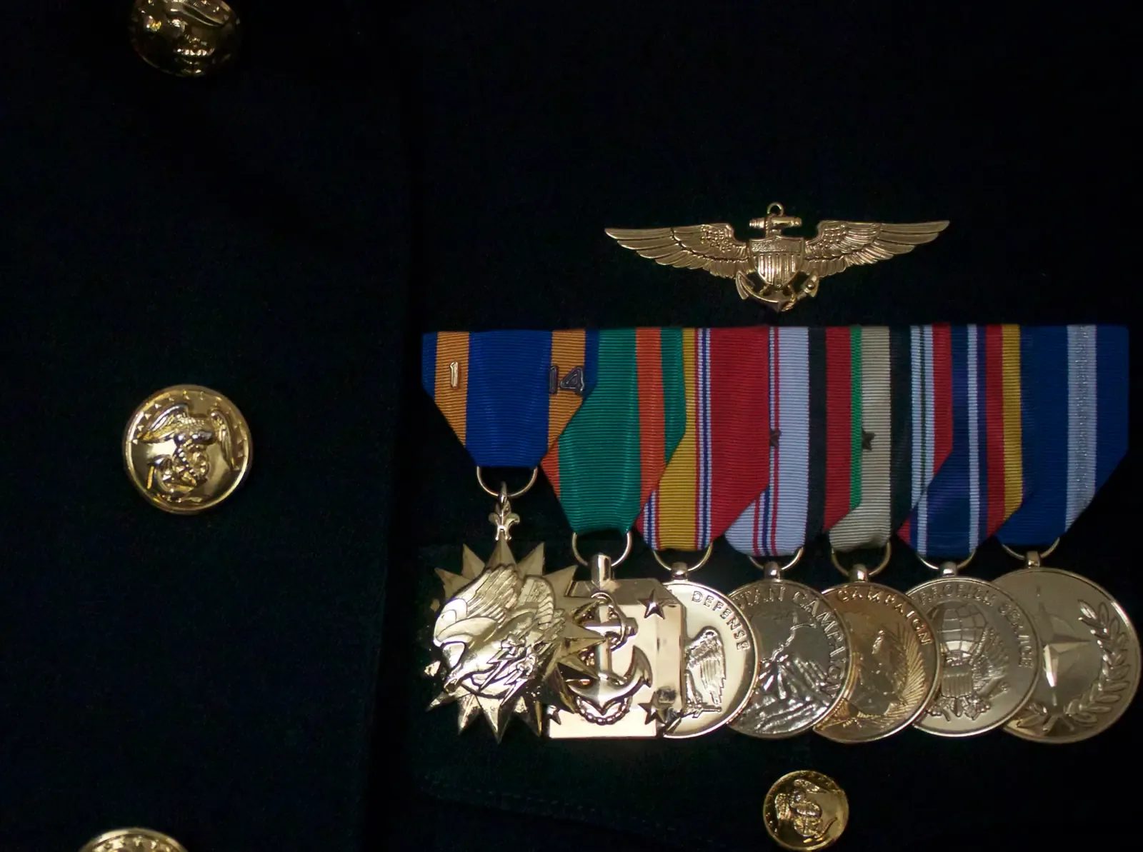 Gold Naval Aviator wings above a row of medals on a Navy dress blue uniform