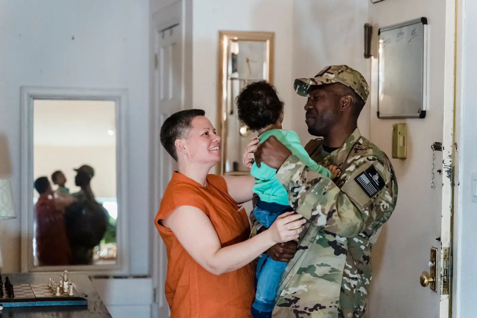Service member in uniform holding a child next to family at home