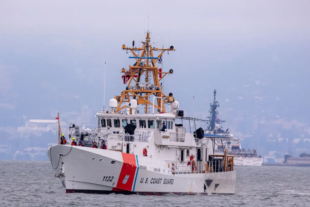 U.S. Coast Guard cutter underway in a bay with a city skyline behind it